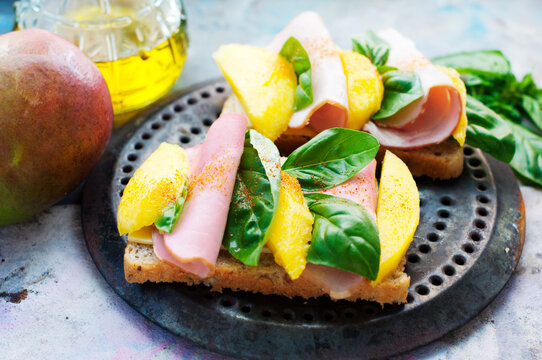 Sandwiches with mango, ham, cream cheese, basil and olive oil on a metal tray