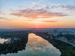 Scenic aerial city sunrise with clouds reflecting in mirror water surface on wide river. Early morning, dawn in Kharkiv Zhuravlivskyy Hidropark from sky. Drone photography