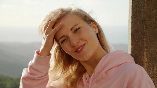 Young blonde woman smiles at the camera on a windy day - people photography in extreme slow motion