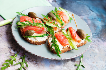 Sandwiches with trout, capers, cucumber, arugula with olive oil on gray plate on gray background