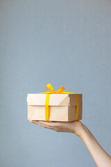 woman's hand holding a kraft cardboard box natural color, woman holding boxes with yellow gift ribbon or wrapping. gift or food delivery, food and clothing delivery, gift wrapping for birthday or