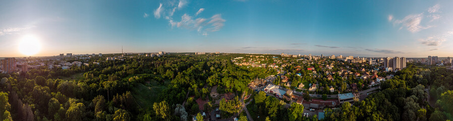Aerial evening wide panoramic view on green summer Kharkiv city recreation park Sarzhyn Yar. Botanical garden playground and church in residential Shatilovka district area in sunset light