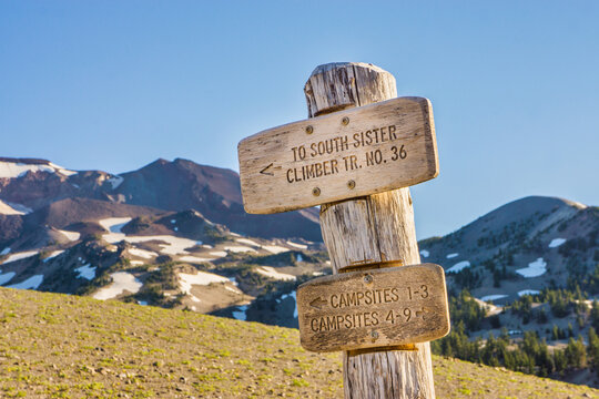 Wooden signpost guides hikers along a trail to a distant volcanic mountain summit peak.