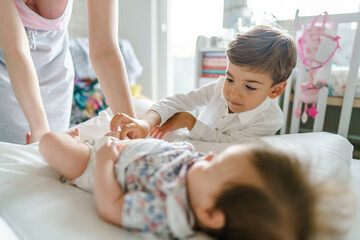 Small caucasian boy four years old helping his mother changing diapers to his small baby brother or...