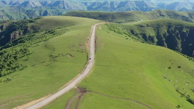 Top view of the mountain road through the green field. Drone footage of the grass field the winding road and driving car