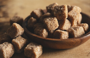 Brown cane sugar cubes in a wooden dish set against a wooden background.