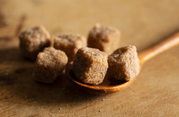Wooden spoon and brown cane sugar cubes on a wooden background.