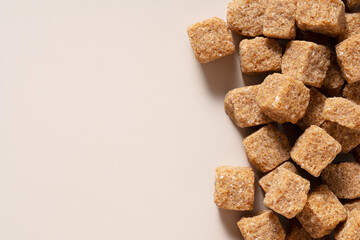 Brown cane sugar cubes placed on a beige background. View from directly above.