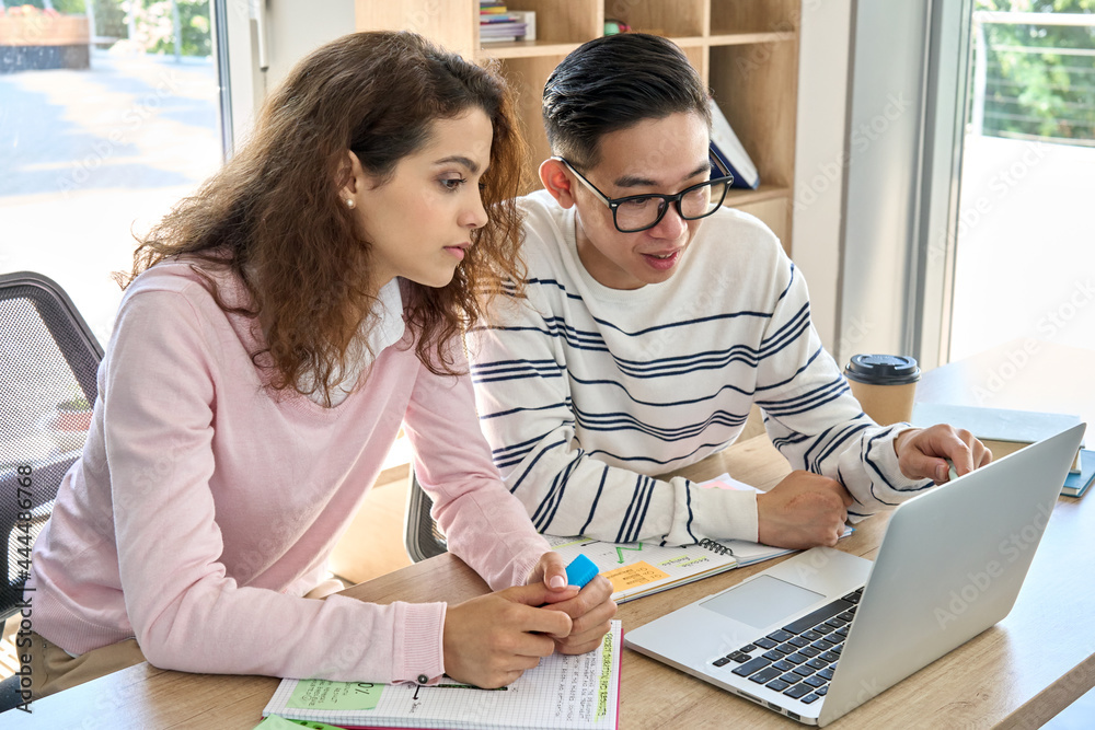 Wall mural gen z latin girl and asian guy classmates talking on class work looking at laptop computer. diverse 