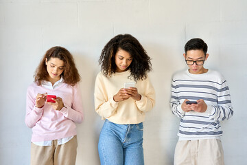 Young teenage cool multiethnic group of gen z high school college students standing on white wall background holding mobile cell phones looking at smartphones using apps. Social media concept - obrazy, fototapety, plakaty