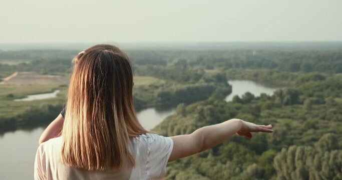 Mother and daughter on the observation deck, mother shows her hand on the woods and the river. A place to relax, walk and play sports.