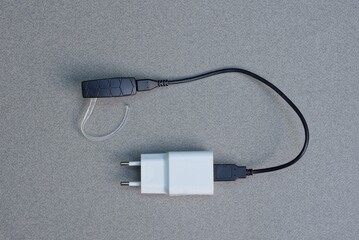 black electrical cable with USB in a white plastic adapter socket with one earphone lies on a gray table