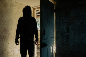 A horror concept. Of a hooded figure with no face standing in the doorway of a decaying room in an...
