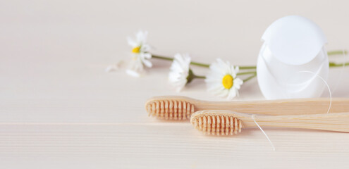 Wooden toothbrushes, dental floss and white daisy flowers on a table