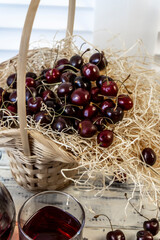 Cherry and cherry juice or wine on a wooden table, a decanter and a glass with juice, a basket with...