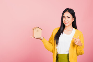 Happy Asian portrait beautiful cute young woman excited smiling holding house model on hand, studio shot isolated on pink background, broker female hold home real estate insurance and banking concept