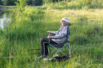 An elderly fisherman on the bank of a quiet river enjoys fishing.