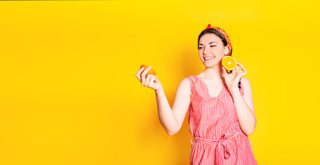 Portrait of a comic happy girl in an orange bandana holding orange halves near her face on a colorful yellow isolated background