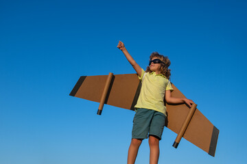 Boy pilot against a blue sky. Cute dreamer boy playing with a cardboard airplane. Childhood....