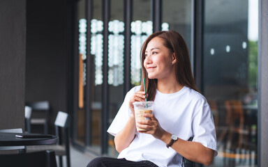 Portrait image of a beautiful young asian woman holding and drinking iced coffee in cafe