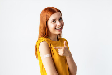 Covid-19 vaccinated caucasian happy smiling young woman showing arm with plaster, gray background
