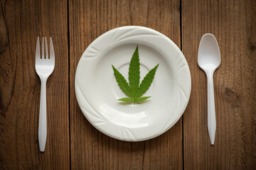 Cannabis leaf - marijuana leaves plant on white plate on the wooden table and spoon fork, cannabis food nature herb concept