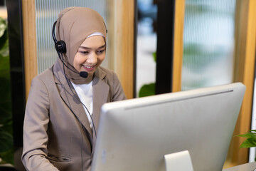 Attractive business Asian woman  muslim in suits and headsets working with desktop computer at ...