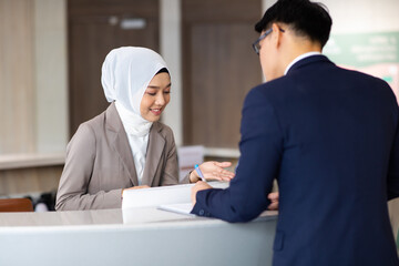 Portrait of muslim woman receptionist at desk in lobby.  Asian business man standing at reception...
