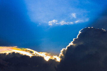 gold rainbow sunset ray behind blue cloudscape