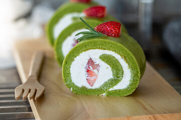 Matcha green tea roll cake with fresh cream topping with strawberry paste on wooden board.