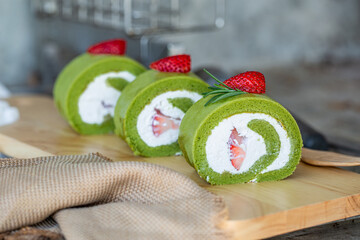 Matcha green tea roll cake with fresh cream topping with strawberry paste on wooden board.