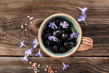 black olives in a ceramic bowl on a wooden background, decorated with blue flowers and himalayan salt, top view, close-up
