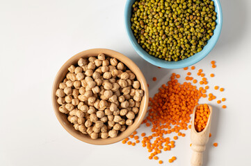 dry chickpeas, orange lentils, green mung bean, in a ceramic dish on a white table