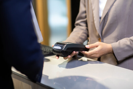 Female receptionist employee holding card reader machine on hand at checkout counter.