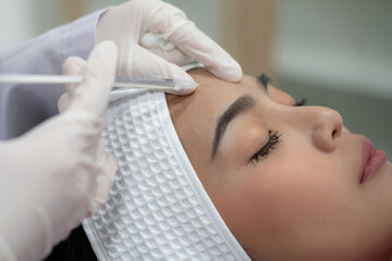 Close up shooting hands holding syringe expert beautician injecting botox in female forehead. She is gently smiling