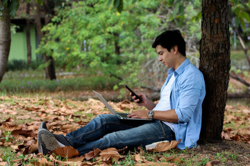 Fototapeta premium Handsome man using smart phone under the tree, Concept of freelance working background.