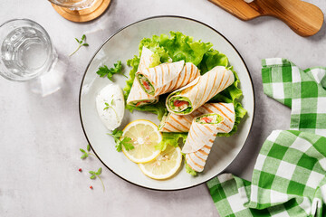 Wrap sandwich, roll with salted salmon fish and fresh vegetables. Light gray background. Top view
