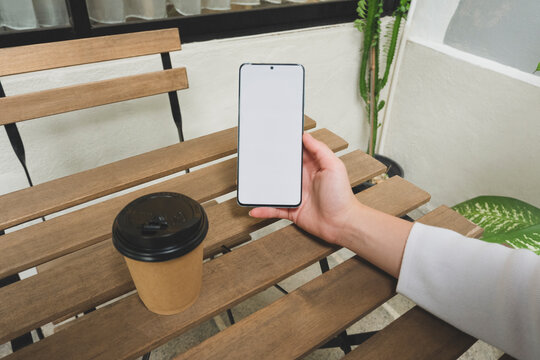 Close up image of a person using a mock up smartphone with blank screen in a coffee shop