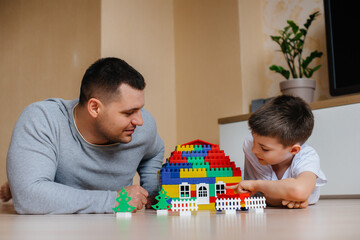 A little boy together with his father is played by a constructor and builds a house. Construction of a family home.