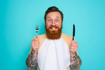 Happy man with tattoos is ready to eat with cutlery in hand