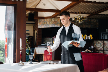 A young male waiter in a stylish uniform is engaged in serving the table in a beautiful gourmet restaurant. Restaurant activity, of the highest level.