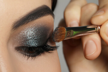 Applying dark eye shadow with brush onto woman's face, closeup. Beautiful evening makeup