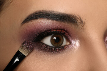Applying dark eye shadow with brush onto woman's face, closeup. Beautiful evening makeup