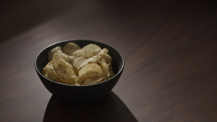 organic potato chips with black pepper in black bowl on walnut table