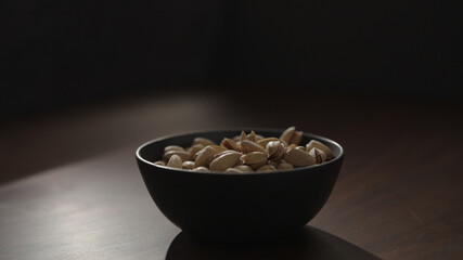 roasted pistachios in black bowl on walnut table
