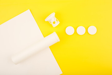 Creative simple flat lay with white opened tube with spilled effervescent vitamins on white and yellow background. Concept of vitamin C, kids vitamins or supplements for energy boosting
