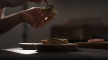 man spread pesto on baguette slices on olive wood board