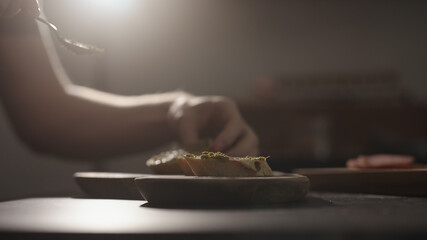 man spread pesto on baguette slices on olive wood board