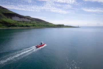 Obraz premium A Red Passenger Ferry Motors Alongside a Beautiful Coastline