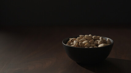 Slow motion handheld shot of roasted pistachios in black bowl on walnut table